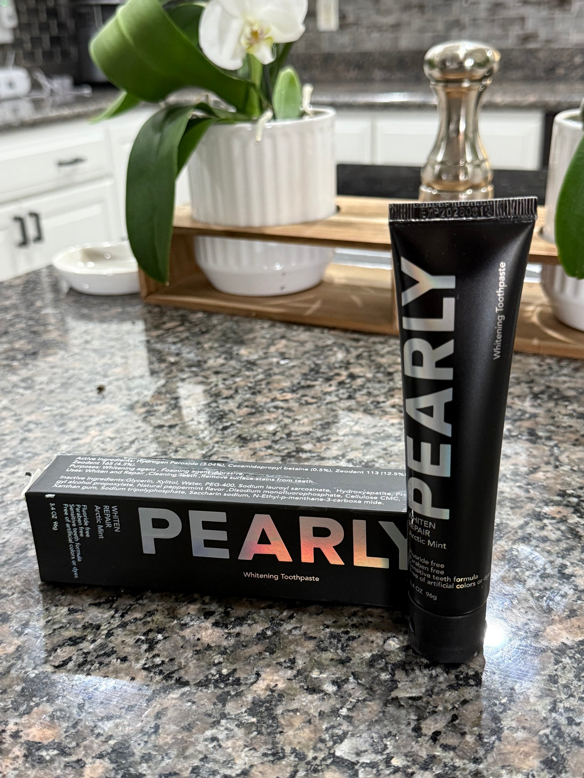 Pearly tube and box on a bathroom counter with a mirror and flowers in the background.