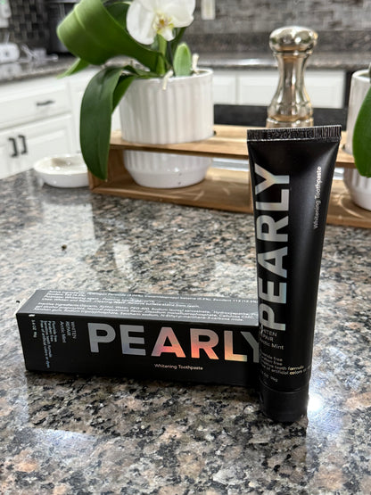 Pearly tube and box on a bathroom counter with a mirror and flowers in the background.