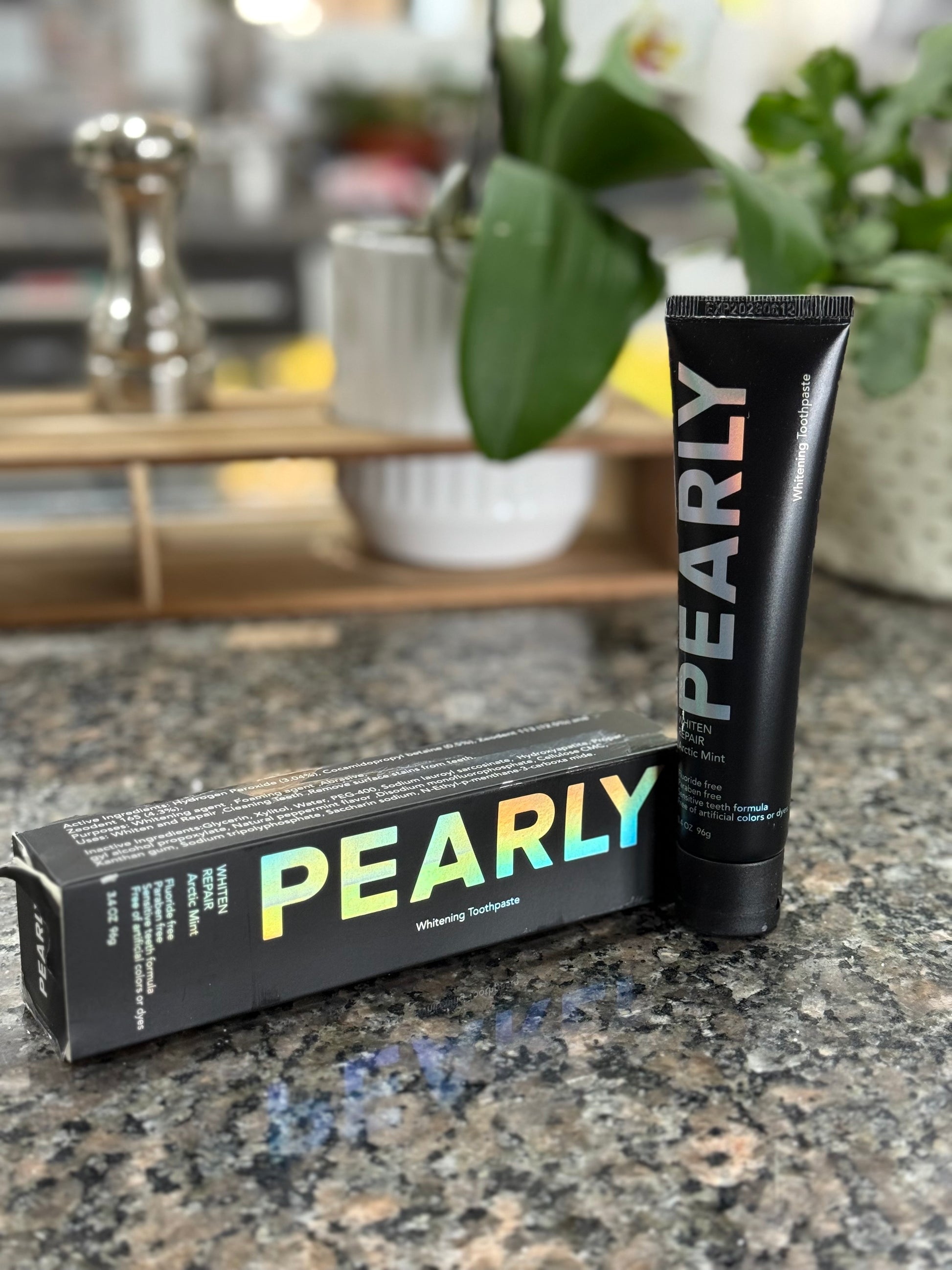 Pearly whitening toothpaste packaging and tube on a countertop with a blurred background